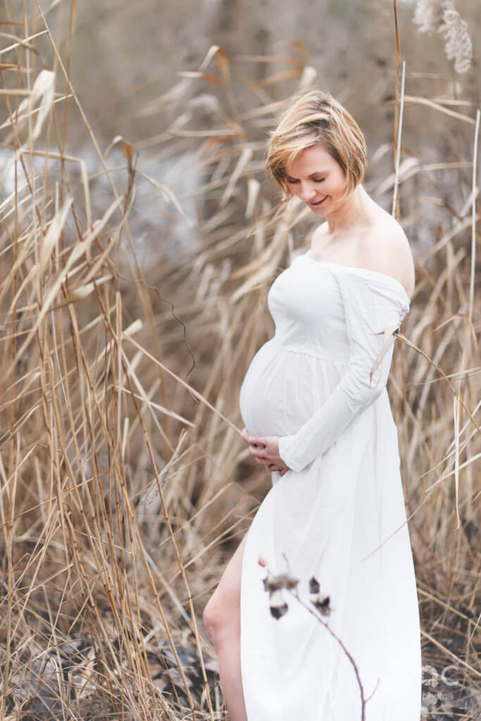 Une future maman rayonnante dans une robe blanche caresse tendrement son ventre arrondi