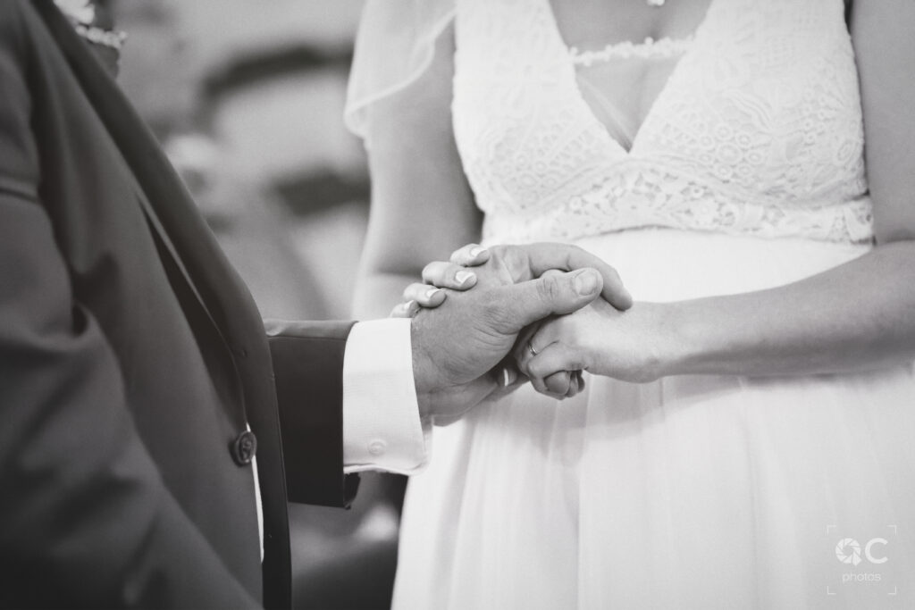 Gros plan en noir et blanc sur deux mains entrelacées des futurs mariés. L'image évoque le thème de l'union, de l'amour et du mariage.